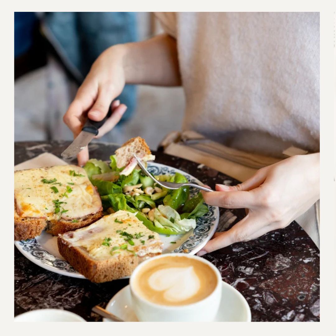 personne à table qui mange un croque monsieur élaboré et un café avec du latte art